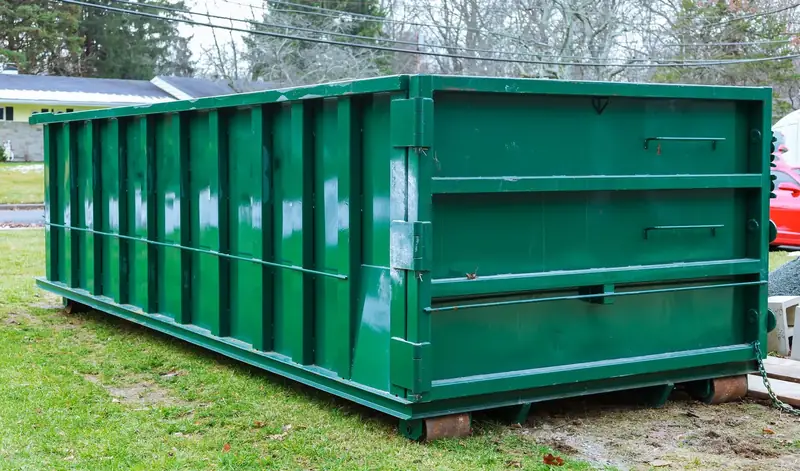 Roll-off dumpster set on wooden boards beside a home